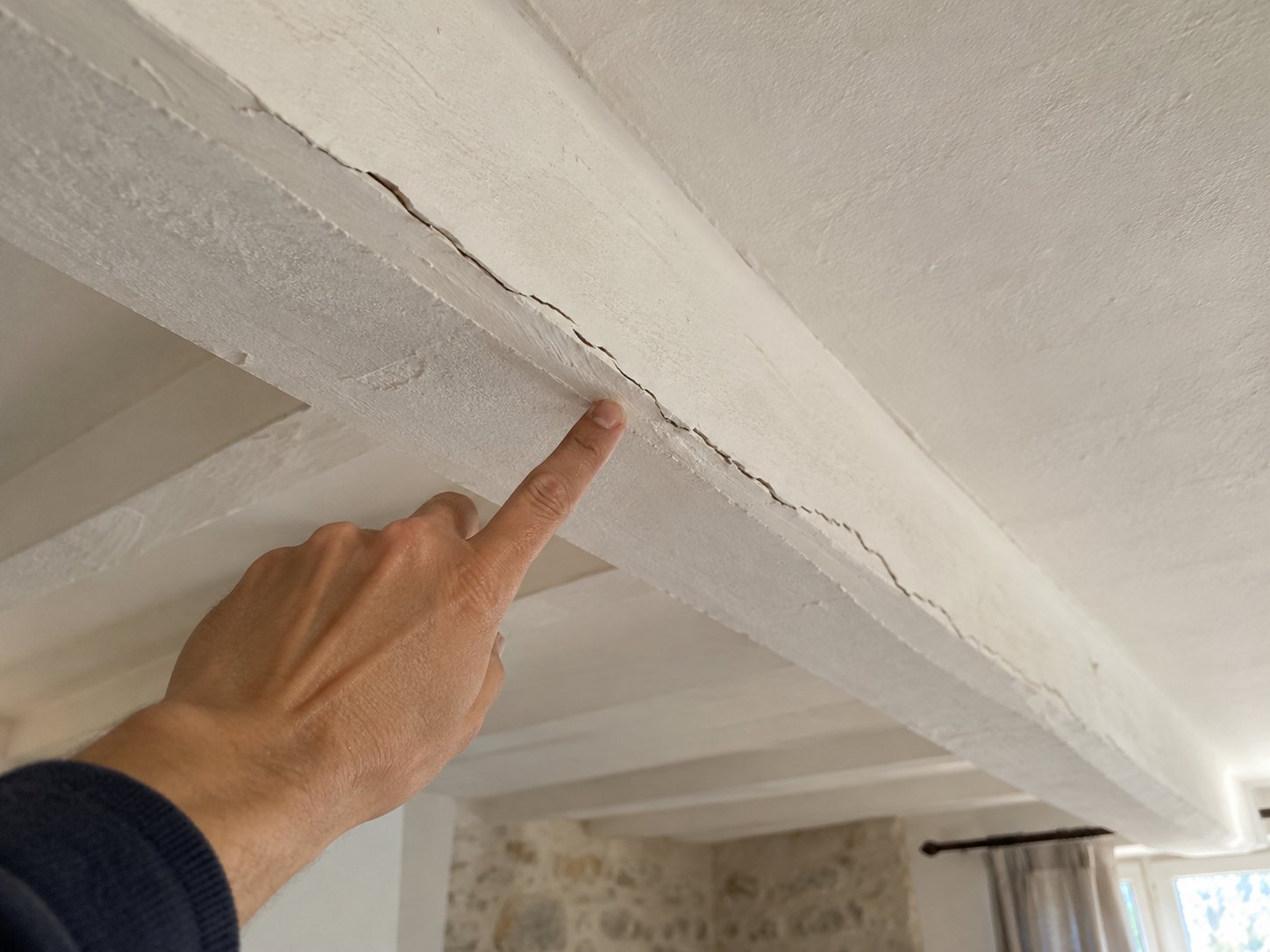 Fissure fine dans l’enduit d’un plafond le long d’une poutre